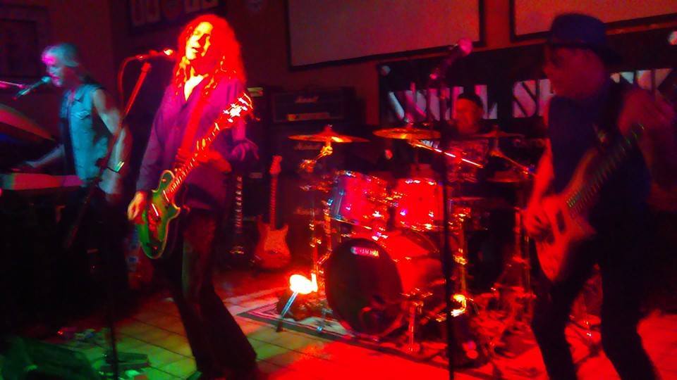 Tucson Bands and Concerts Guide (Mar 13–19, 2026) 3 Shell Shock performing live at Big Bad Wolf in Tucson during a Tucson bands and concerts show with guitar, bass, keyboard, and drums under red stage lights.