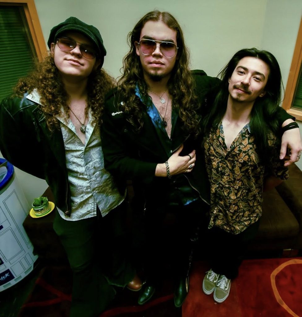 Tucson Band Spotlight: Znora 5 Three members of Znora standing together indoors in a backstage setting before a live performance