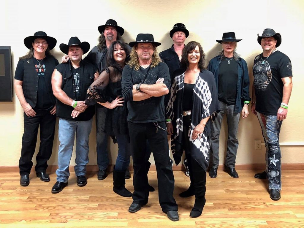 Tucson Musician Spotlight: Mark Holladay 6 Members of the Tucson-based Southern rock tribute band Mr. Skynyrd pose together for a group photo in 2018. The band is dressed in black attire and cowboy hats, with keyboardist Mark Holladay standing near the right side of the group. The musicians gather indoors before a performance, representing one of Tucson's longtime Lynyrd Skynyrd tribute acts.
